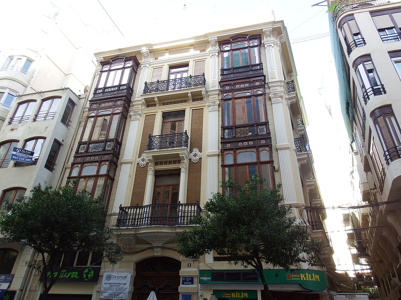Edificio residencial modernista con miradores y balcones en una calle arbolada de Valencia